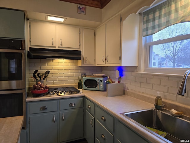 kitchen with under cabinet range hood, stainless steel appliances, a sink, and light countertops