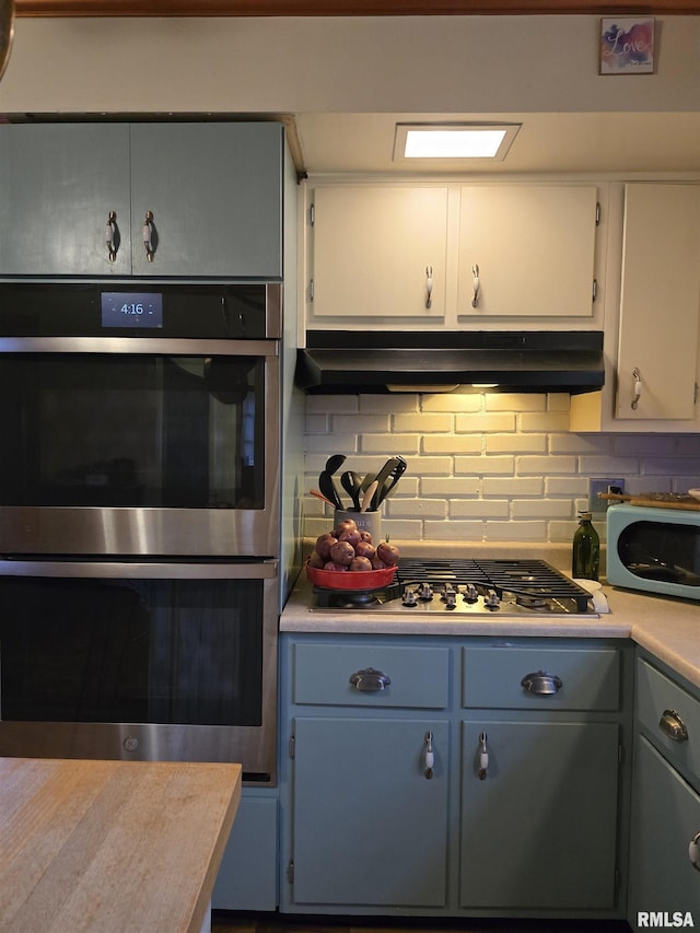 kitchen with under cabinet range hood, white cabinets, light countertops, appliances with stainless steel finishes, and decorative backsplash