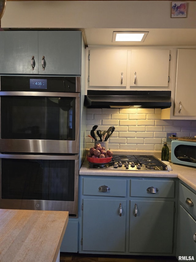 kitchen featuring under cabinet range hood, appliances with stainless steel finishes, light countertops, and decorative backsplash