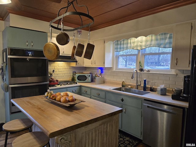 kitchen with butcher block counters, appliances with stainless steel finishes, ornamental molding, a sink, and backsplash