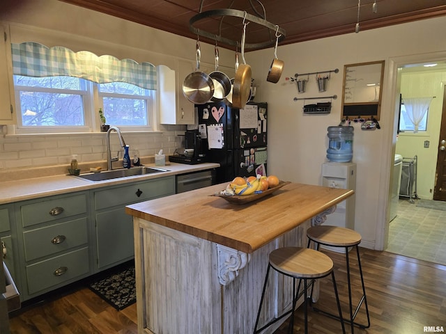 kitchen with butcher block countertops, a breakfast bar, a sink, green cabinets, and decorative backsplash