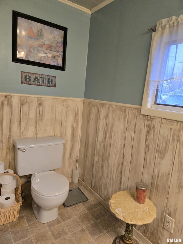 bathroom with toilet, a wainscoted wall, and tile patterned flooring