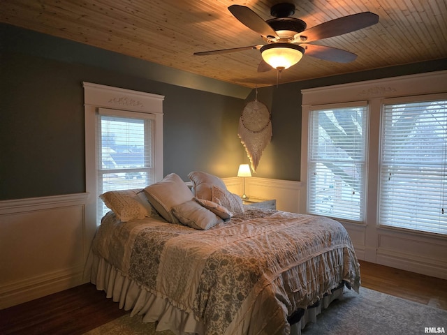 bedroom with wooden ceiling, a wainscoted wall, a decorative wall, and wood finished floors