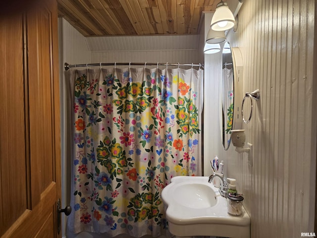 bathroom featuring a shower with shower curtain, a sink, wood ceiling, and wooden walls