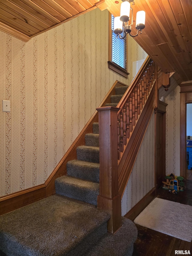 staircase with a chandelier, wood finished floors, wood ceiling, and wallpapered walls