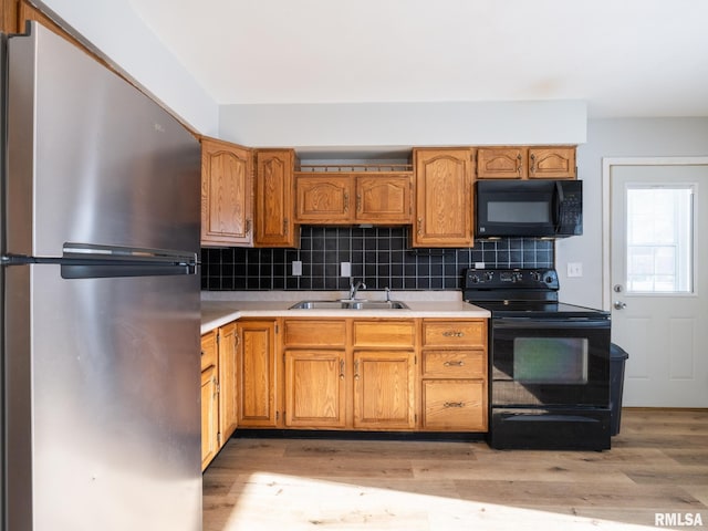 kitchen featuring tasteful backsplash, light wood finished floors, light countertops, black appliances, and a sink