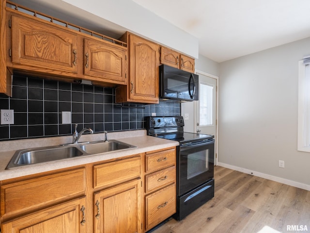 kitchen featuring light wood-type flooring, light countertops, decorative backsplash, black appliances, and a sink