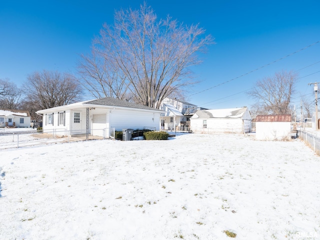 snow covered rear of property featuring a storage unit, an outdoor structure, a garage, and fence