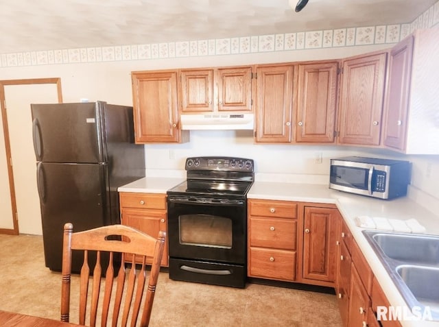 kitchen with light countertops, brown cabinetry, a sink, under cabinet range hood, and black appliances