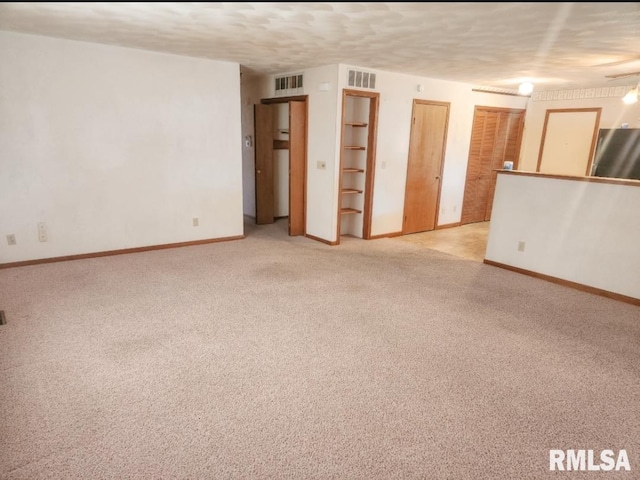 spare room with light carpet, a textured ceiling, visible vents, and baseboards