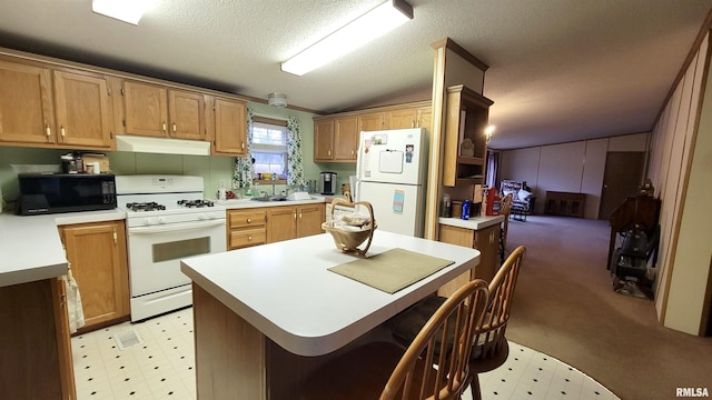 kitchen with light countertops, light floors, a textured ceiling, under cabinet range hood, and white appliances