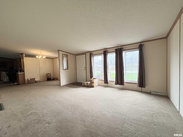 unfurnished living room with a textured ceiling, visible vents, ornamental molding, carpet floors, and an inviting chandelier