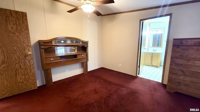 unfurnished bedroom featuring dark colored carpet, ornamental molding, a sink, connected bathroom, and ceiling fan