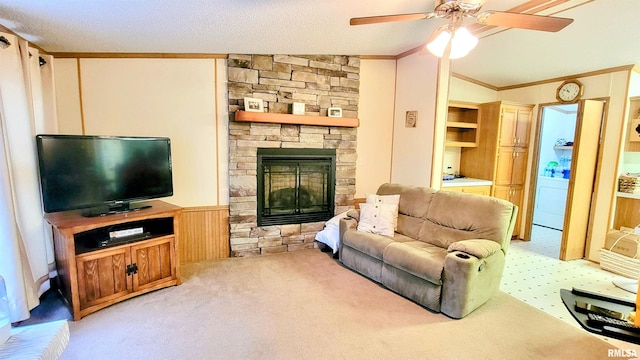 living area featuring ornamental molding, carpet, a wainscoted wall, a ceiling fan, and a stone fireplace