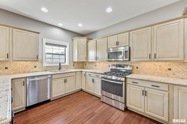 kitchen featuring wood finished floors, recessed lighting, a sink, cream cabinetry, and appliances with stainless steel finishes