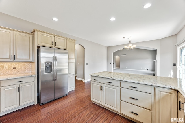 kitchen with dark wood-type flooring, cream cabinetry, arched walkways, stainless steel fridge with ice dispenser, and decorative backsplash