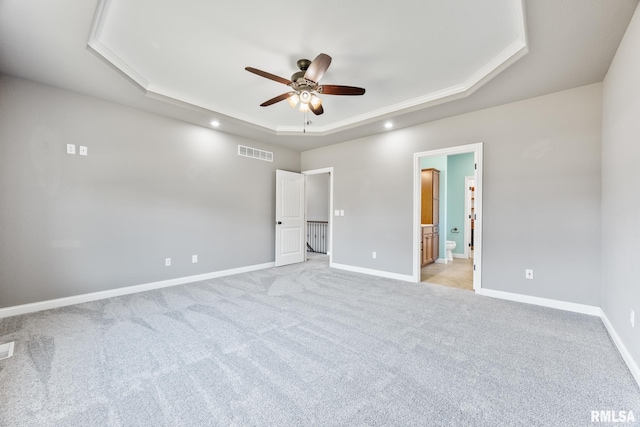 unfurnished bedroom with visible vents, baseboards, light colored carpet, ensuite bath, and a raised ceiling