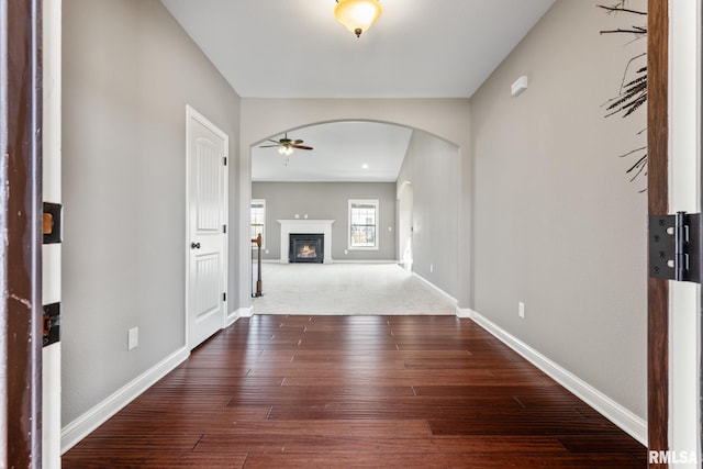 foyer with ceiling fan, baseboards, dark wood-style floors, arched walkways, and a glass covered fireplace