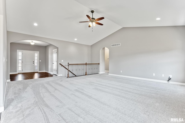 unfurnished room featuring visible vents, arched walkways, dark carpet, and vaulted ceiling