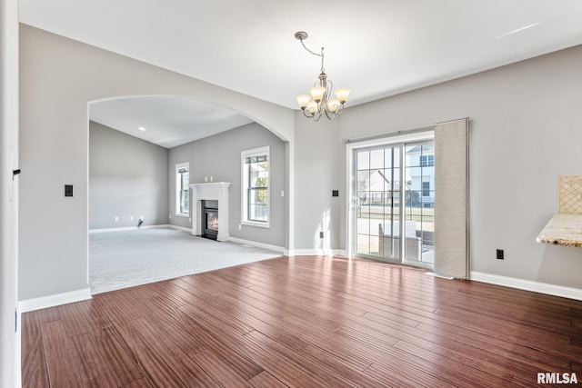 unfurnished living room featuring a fireplace with flush hearth, baseboards, an inviting chandelier, and wood finished floors