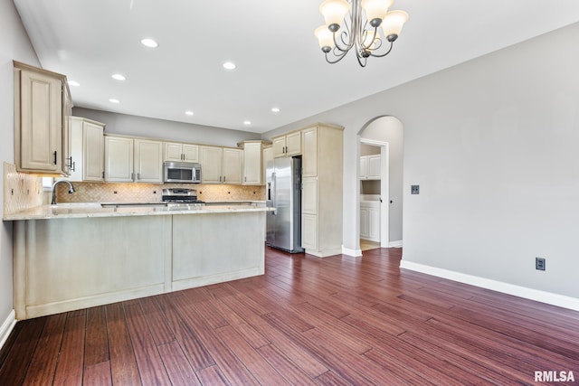 kitchen with cream cabinets, arched walkways, appliances with stainless steel finishes, a peninsula, and decorative backsplash