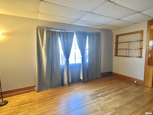 empty room with baseboards, a drop ceiling, and wood finished floors