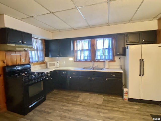 kitchen featuring white appliances, wood finished floors, a paneled ceiling, under cabinet range hood, and a sink