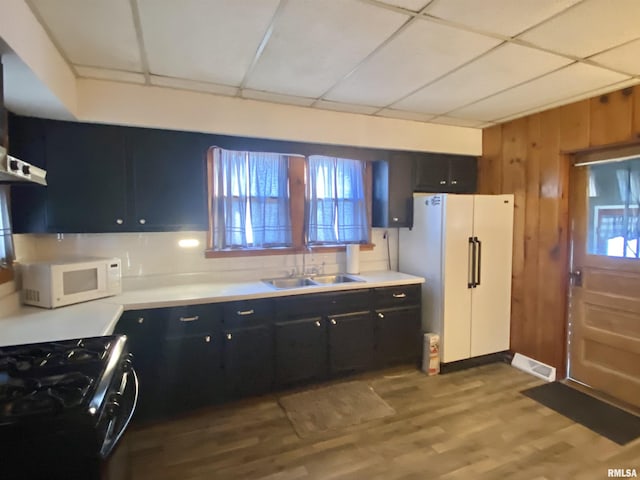 kitchen with dark cabinets, white appliances, a sink, and wood finished floors