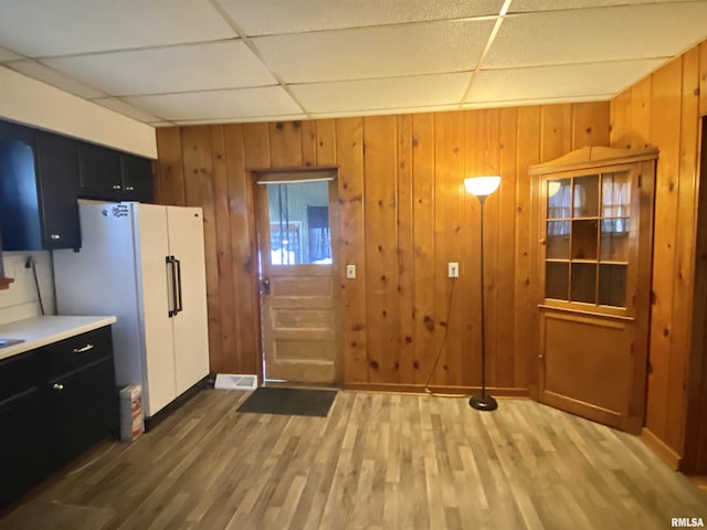 kitchen featuring a drop ceiling, wood finished floors, freestanding refrigerator, and dark cabinets