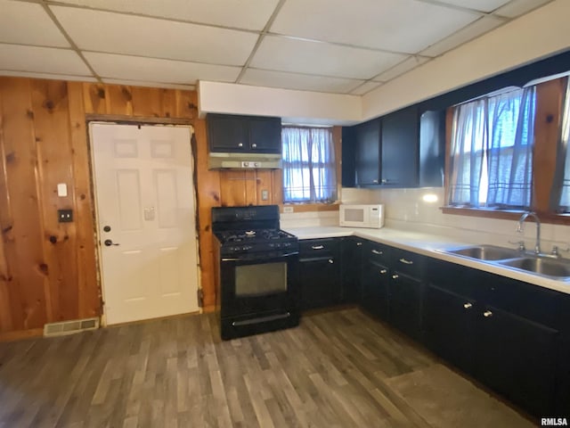 kitchen featuring black gas range, white microwave, dark cabinetry, under cabinet range hood, and a sink