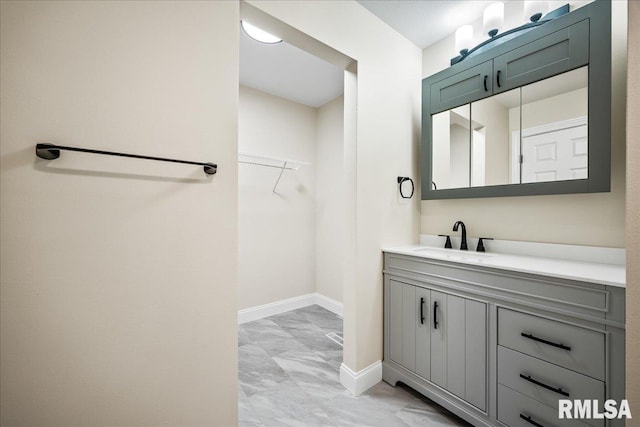 bathroom with a walk in closet, marble finish floor, vanity, and baseboards