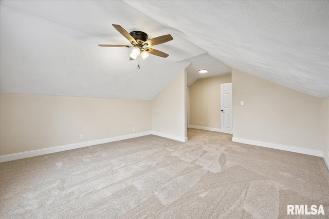 additional living space with light carpet, vaulted ceiling, a textured ceiling, ceiling fan, and baseboards