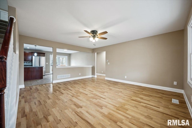 unfurnished living room with light wood-type flooring, ceiling fan, visible vents, and baseboards