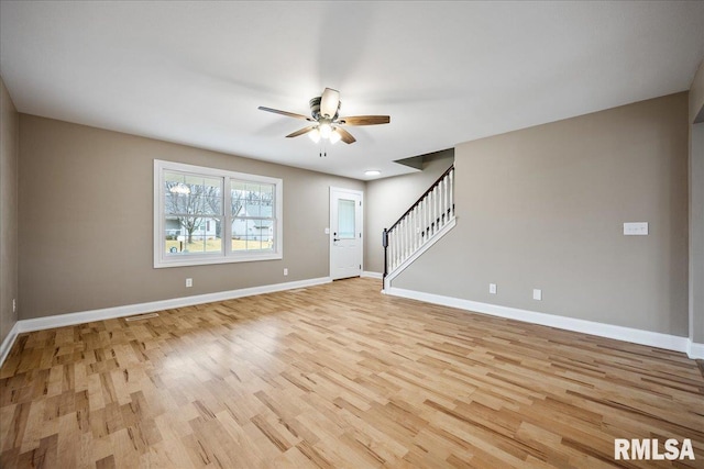 spare room featuring a ceiling fan, light wood-type flooring, stairway, and baseboards