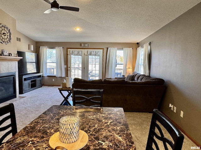 living area featuring visible vents, a tile fireplace, lofted ceiling, a textured ceiling, and carpet flooring