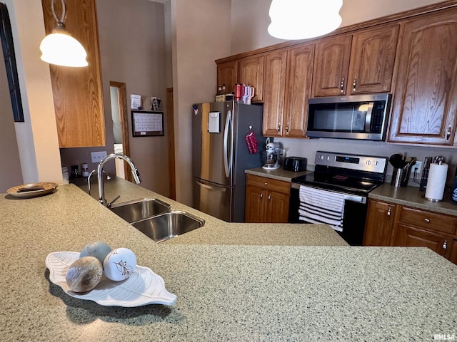 kitchen with brown cabinetry, appliances with stainless steel finishes, decorative light fixtures, light stone countertops, and a sink