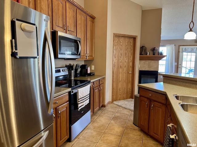 kitchen featuring light tile patterned floors, brown cabinetry, appliances with stainless steel finishes, hanging light fixtures, and a fireplace