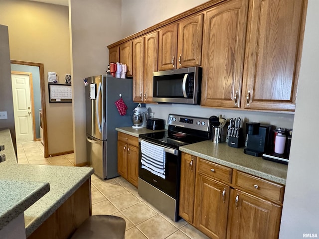 kitchen with light tile patterned floors, appliances with stainless steel finishes, and brown cabinetry