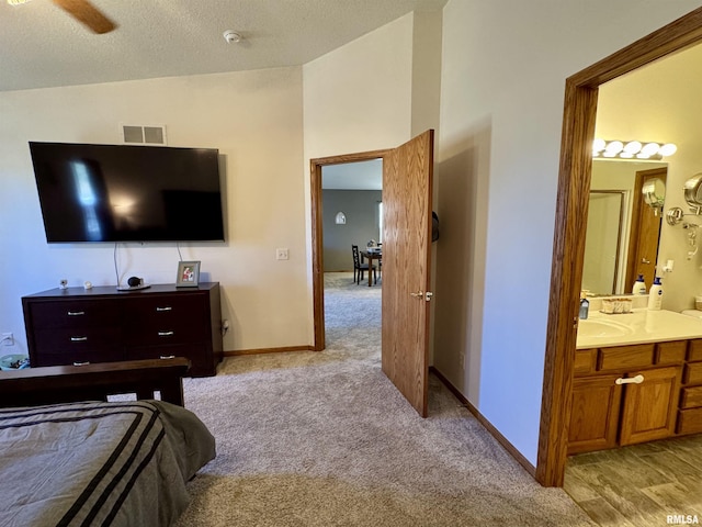 bedroom featuring light carpet, a sink, visible vents, baseboards, and ensuite bath