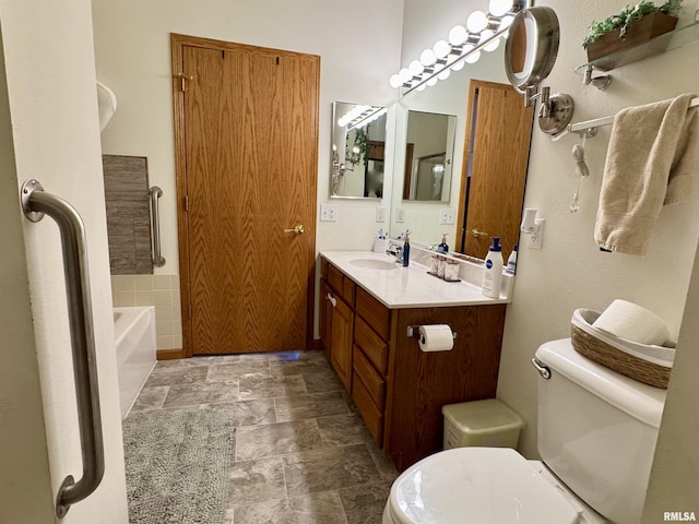 bathroom with stone finish flooring, a bathing tub, vanity, and toilet