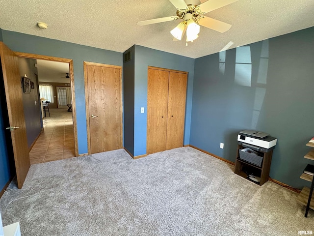 carpeted bedroom with multiple closets, ceiling fan, a textured ceiling, tile patterned flooring, and baseboards