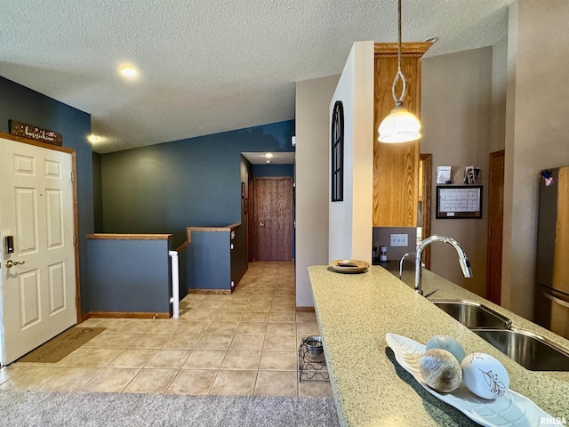 kitchen featuring light tile patterned floors, lofted ceiling, freestanding refrigerator, a textured ceiling, and a sink