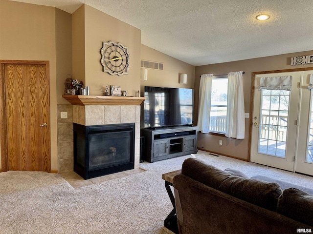 carpeted living area with lofted ceiling, a textured ceiling, visible vents, baseboards, and a tiled fireplace