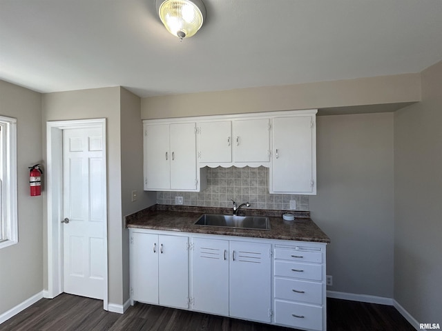 kitchen featuring dark countertops, tasteful backsplash, a sink, white cabinetry, and dark wood-style flooring