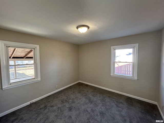 empty room featuring plenty of natural light, baseboards, and dark colored carpet