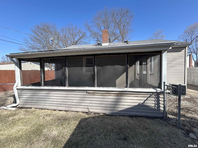 rear view of house featuring fence, a chimney, and a sunroom