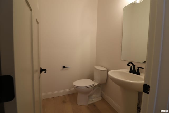 half bathroom with a sink, wood finished floors, toilet, and baseboards