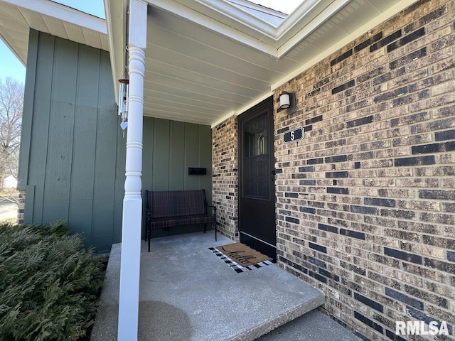 doorway to property featuring a porch and brick siding