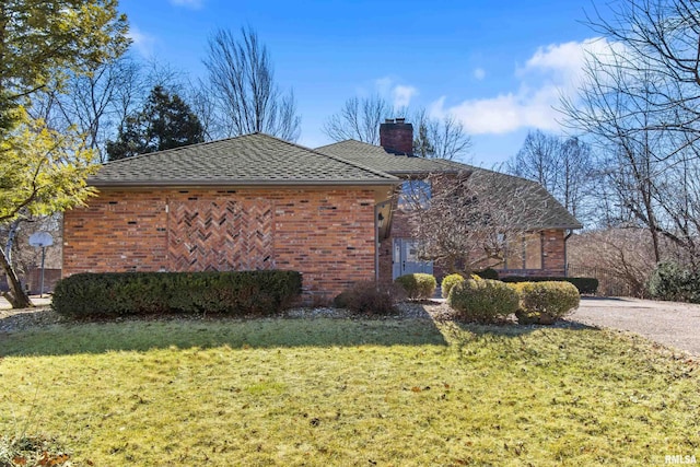 view of side of home featuring a shingled roof, a lawn, brick siding, and a chimney