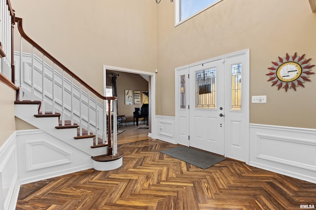 entrance foyer with stairway, a wainscoted wall, and a towering ceiling